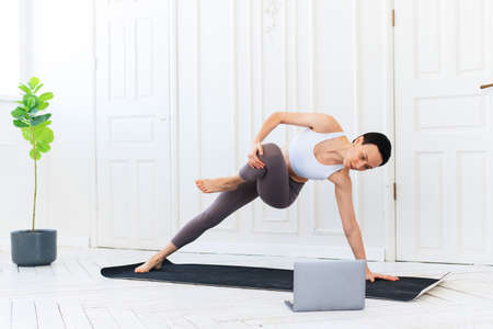 Fitness and yoga trainer teaches via laptop. Online Training. Fit Young Woman Excersising At Home, Watching Video Tutorial On Laptopの写真素材