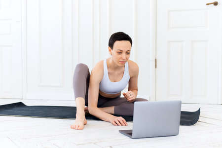 Beautiful adult woman doing sports, stretching and yoga on the mat at home. Quarantined sports during the coronavirus lockdownの写真素材