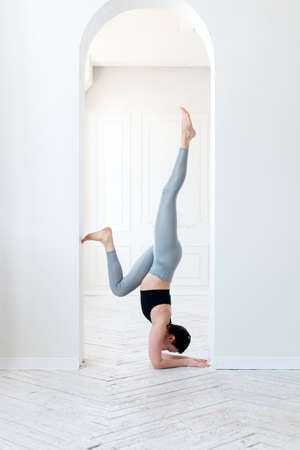 A young woman practices yoga and stands on her arms in the arch of a bright room. Young attractive yogi woman practicing yoga conceptの写真素材
