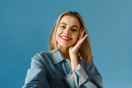 Lovely young woman makes selfie on a blue background in the studioの写真素材