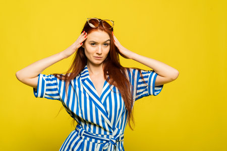 Beautiful stylish young woman wears yellow sunglasses, enjoys summer rest, has fun expression on face, poses in studioの写真素材