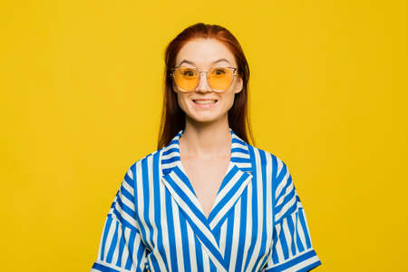 Funny cheerful woman in yellow sunglasses and blue overalls on a yellow background. Looking at camera, copy spaceの写真素材