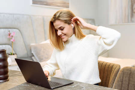 A young woman works with a laptop in her apartment. Freelance businesswoman in headphones is holding a business meeting from homeの写真素材