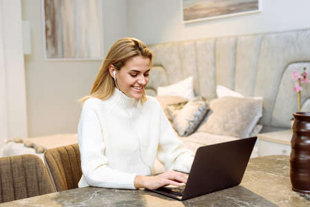 A young woman sits at the table at home and works in a laptop. Businesswoman freelancerの写真素材