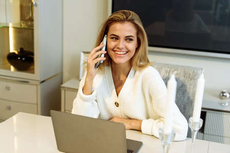 A woman works from home on a laptop and speaks on the phone with a business partner or bossの写真素材