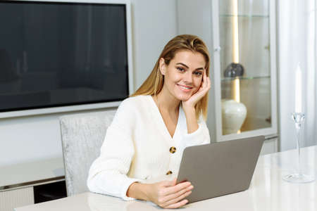A young woman sits at the table at home and works in a laptop. Businesswoman freelancerの写真素材