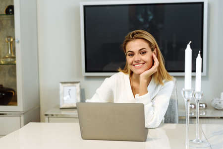 Young woman using computer laptop in her living room and looking at the camera. Female freelancer working at homeの写真素材