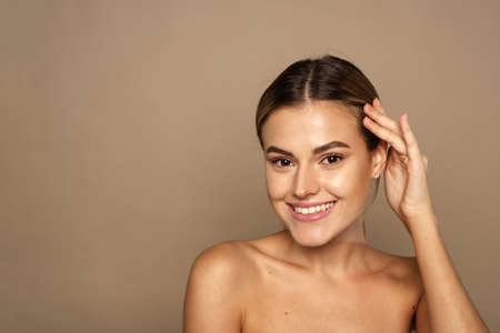Toothy smiling young woman with shiny glowing perfect facial skin and bare shoulder looking to cameraの写真素材