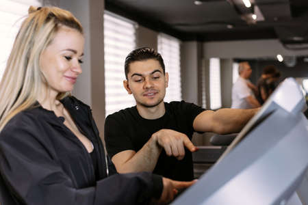 A young male trainer shows a woman how to use a treadmill correctly in a gymの写真素材