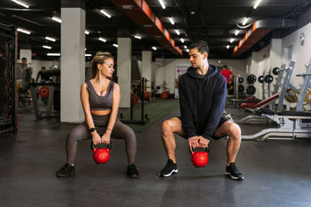 Personal trainer shows a woman how to squat with a kettlebell in a sports backgroundの写真素材