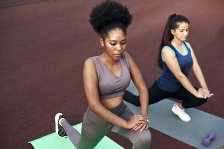 Two lovely young women stretching while standing on yoga mats before training outdoorsの写真素材