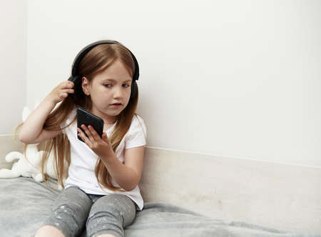 A girl of preschool age communicates on social networks, sitting on her bed next to toysの写真素材