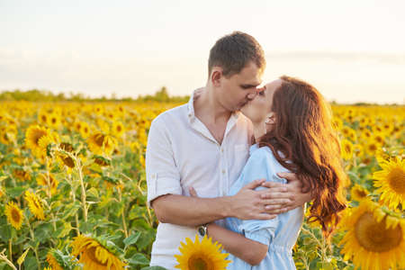 Smiling happy couple hugging in the middle of a field with sunflowers. Sun glare. Romantic Couple on a Love Momentの写真素材