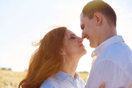 Smiling happy couple. Handsome Caucasian guy wearing white shirt gentle hugs a smiling girl with blond hair in dress.の写真素材