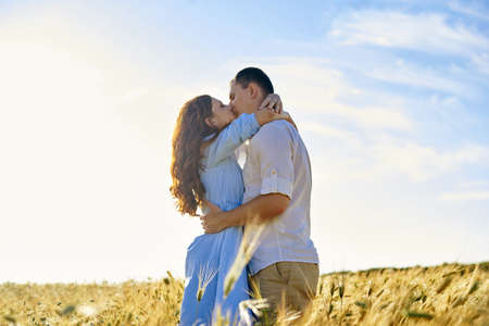 Stylish and modern couple kissing in a wheat field. A young woman hugs her boyfriend and kisses each other. The concept of passion and loveの写真素材
