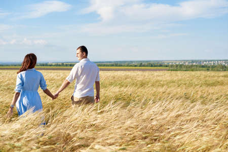 Happy couple holding hands walking through a meadow. The concept of love, good relationships, understanding and harmonyの写真素材