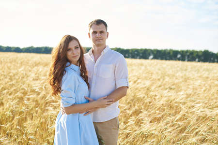 A young couple of lovers women and men hug in nature, in a yellow wheat field. The concept of love, good relationships, understanding and harmonyの写真素材