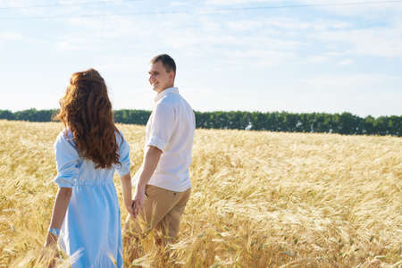 Happy couple holding hands walking through a meadow. The concept of love, good relationships, understanding and harmonyの写真素材
