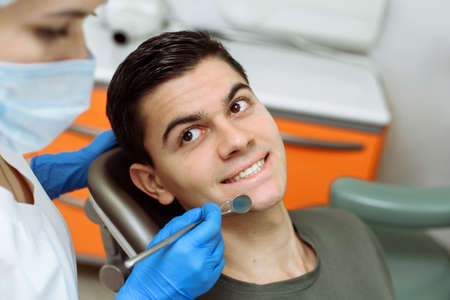 Male young patient sits in the dentists chair while checking teeth, smiles and looks at the doctor. Handsome man happy at the dentist appointmentの写真素材