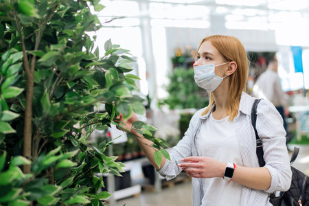 Buying home plants. Choosing trees for the garden. A young woman chooses large deciduous plants for her homeの写真素材