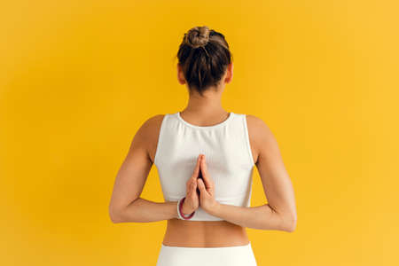 Close up of young woman joining hands behind her back while doing yoga exercise. Young attractive yogi woman practicing yoga, making Namaste behind the backの写真素材