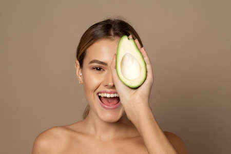 Beautiful woman covers half of her face with half an avocado. Beauty and skin care conceptの写真素材