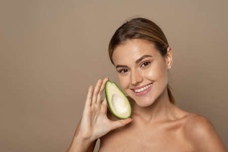 Young smiling brunette holding half a juicy avocado. The concept of cosmetics from natural ingredientsの写真素材