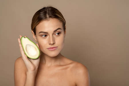 A beautiful woman holds half an avocado in front of her face. Photo of an attractive woman with...