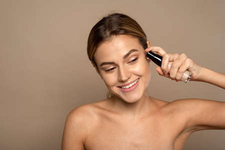 A beautiful smiling model applies foundation from a glass tube. Applying makeup to the face, smoothing the skinの写真素材