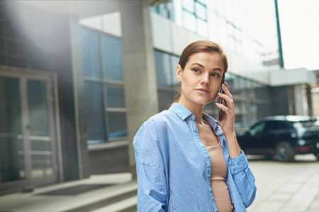 A businesswoman walks against the backdrop of an office center and speaks on the phone. Communication with business partners at a distance. Copy spaceの写真素材