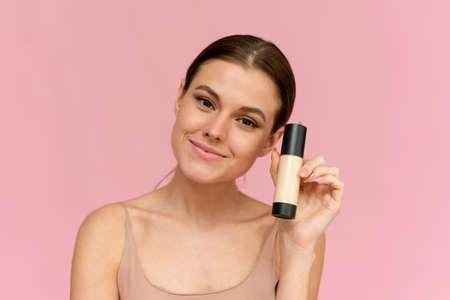 A young woman holds a foundation in a tube on a pink background. Makeup advertisingの写真素材