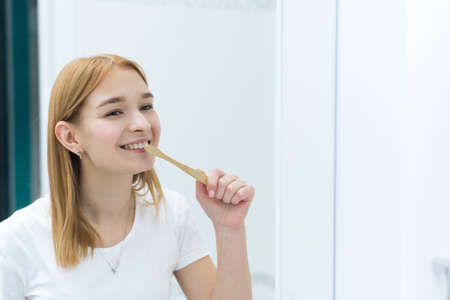 Woman brushing her teeth with bamboo brush in bathroom. Eco friendly brushの写真素材