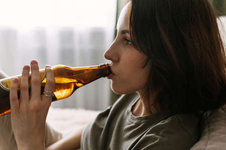 Young woman is drinking beer while sitting on the couch. Female alcoholismの写真素材