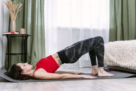 Yoga and sports at home. A young woman performs a shoulder bridgeの写真素材