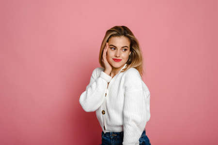 A cute fashion model in a white sweater smiles and looks at the camera against a pink background. Tenderness and youthの写真素材
