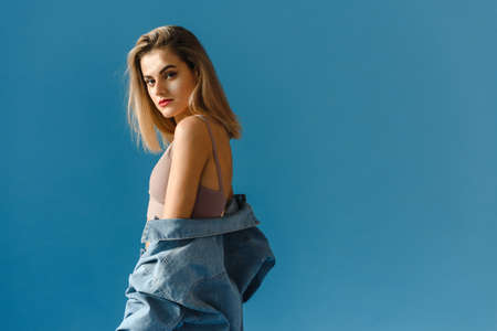 Portrait of a fashionable young woman in a denim jacket, and jeans on a blue backgroundの写真素材
