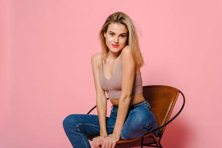 Attractive woman in casual clothes. Fashionable woman-model posing on the chair, studio photography