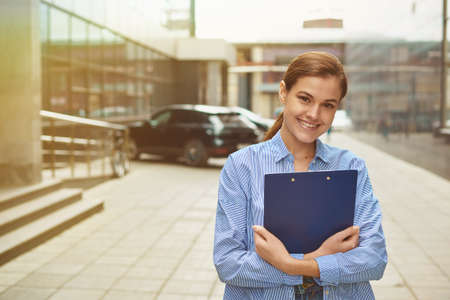 Young female businesswoman holding a tablet with documents at hand and looking at the camera,...