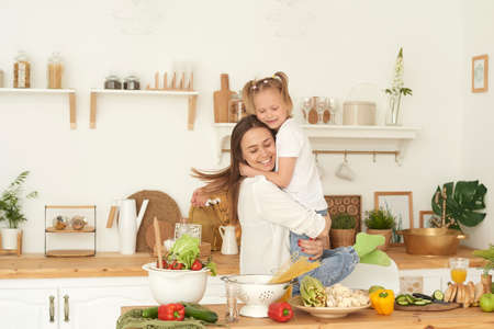 Happy family healthy life concept. Mom hugs her daughter in the kitchen while cookingの写真素材