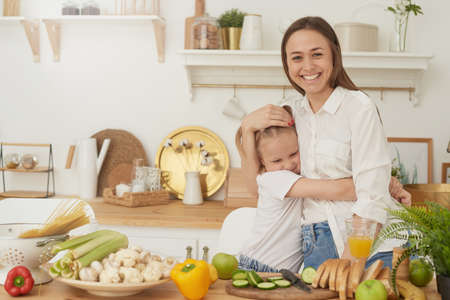 Healthy food at home. A cheerful mother laughs, has fun and hugs her daughterの写真素材