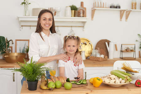Mom and daughter are standing in the kitchen of the house, looking at the camera and laughing. Proper nutrition at home. Spending time togetherの写真素材
