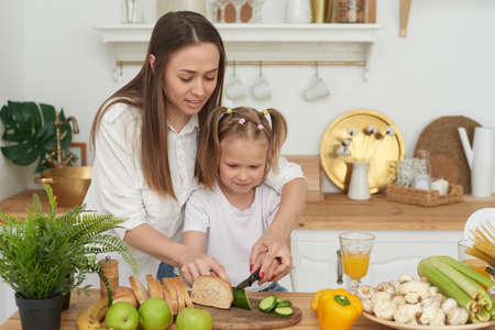 Mom controls her daughters cutting vegetables. Cooking trainingの写真素材
