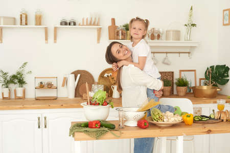 Healthy food at home. A cheerful mother laughs, has fun and hugs her daughterの写真素材
