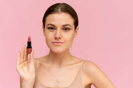 Beautiful woman demonstrating lipstick while standing at isolated pink backgroundの写真素材