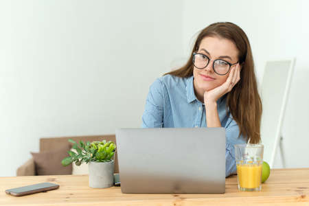 Student thinking while doing complicated homework on line with a laptop at home. Photo of young pretty businesswoman sit indoors in office using laptop computer staring thoughtfully into the airの写真素材