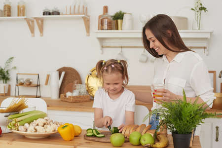 Mom controls her daughters cutting vegetables. Cooking trainingの写真素材