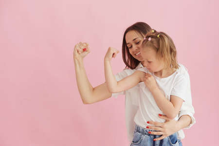 Funny family on the background of a bright pink wall. Mother and her daughter little girl having fun, showing that the strength of the muscles. Feminine power, feminismの写真素材