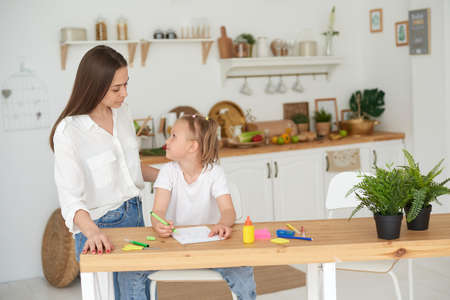 Tutor and child doing homework at kitchen. Mom and daughter are trying to solve the task. They are in a good mood and smileの写真素材