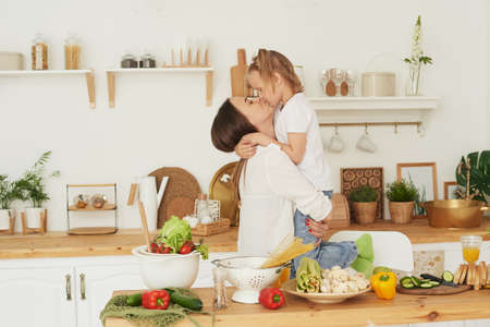 Mom kisses her daughter in the kitchen. Happy family at home. Family healthy life conceptの写真素材