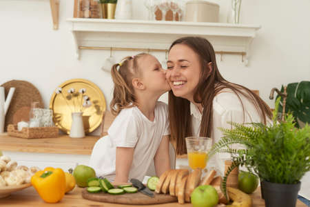 Mom kisses her daughter in the kitchen. Happy family at home. Family healthy life conceptの写真素材